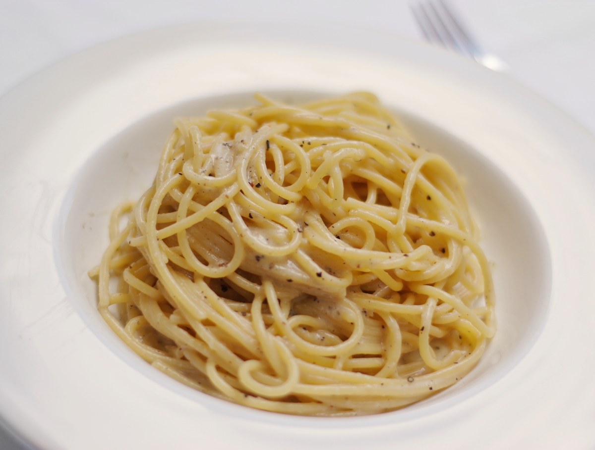Spaghetti cacio e pepe mantecati in un piatto bianco, con pepe macinato