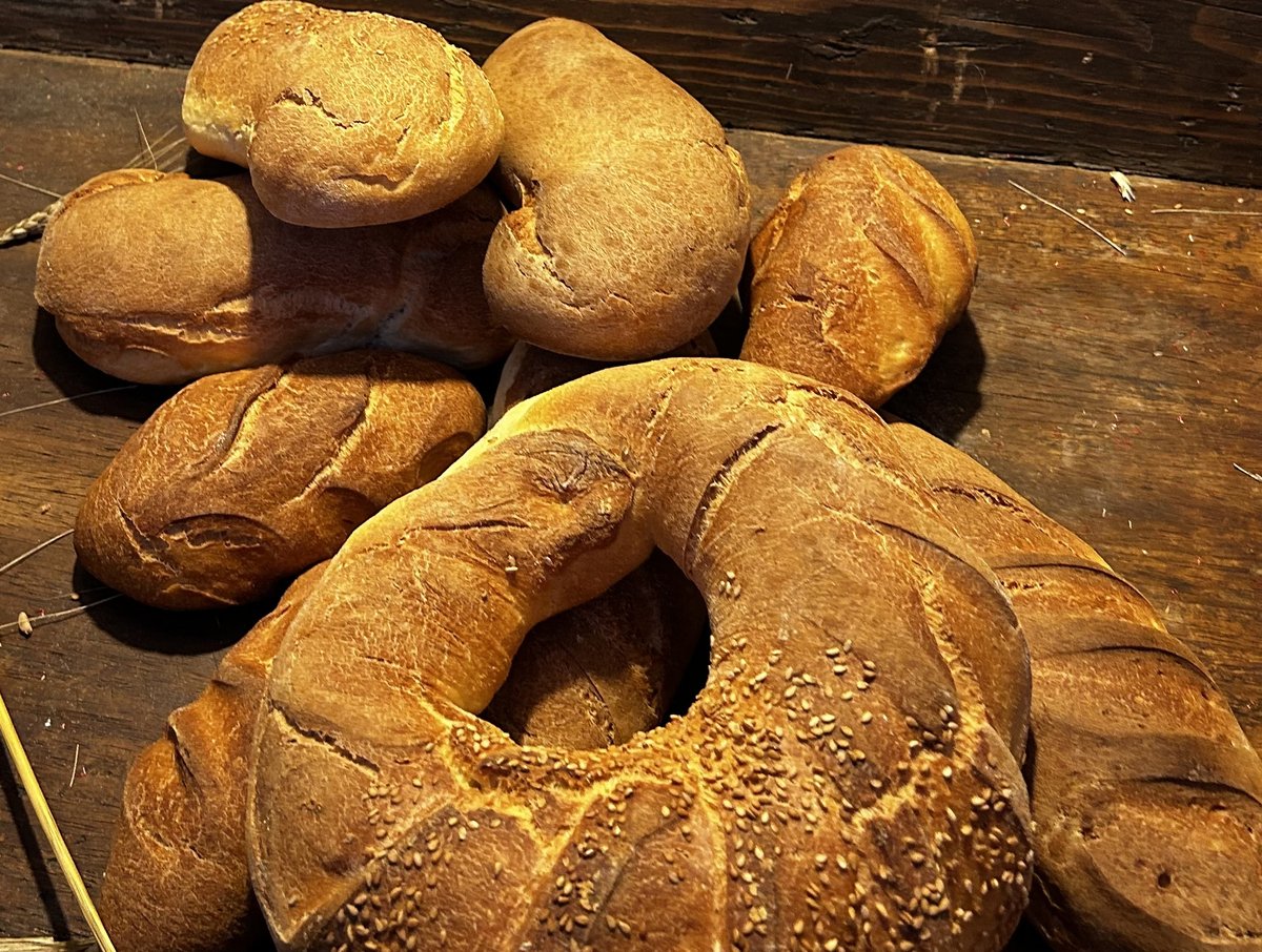 Pane casereccio appena sfornato: filoni, panini e una ciambella al sesamo su un tavolo di legno